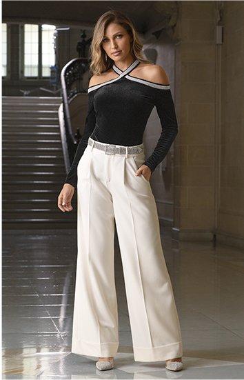 model wearing a black jewel embellished crisscross off-the-shoulder long-sleeve top, silver rhinestone embellished belt, white wide-leg high-waisted pants, and silver rhinestone heels.