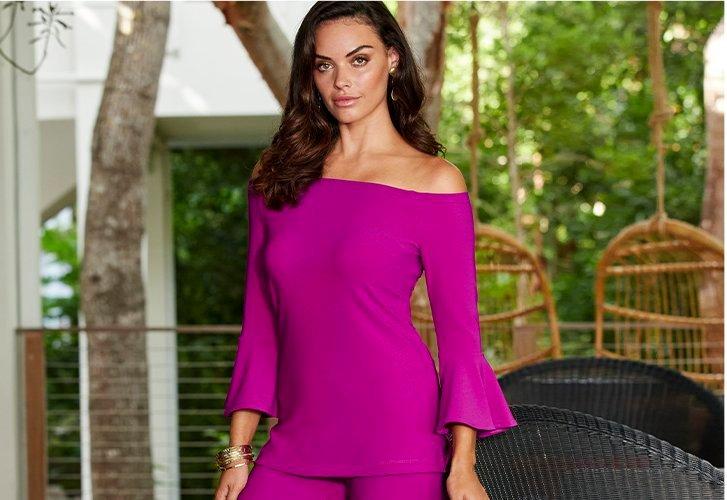 model wearing a bright purple off-the-shoulder flare-sleeve long-sleeve top and matching pants.