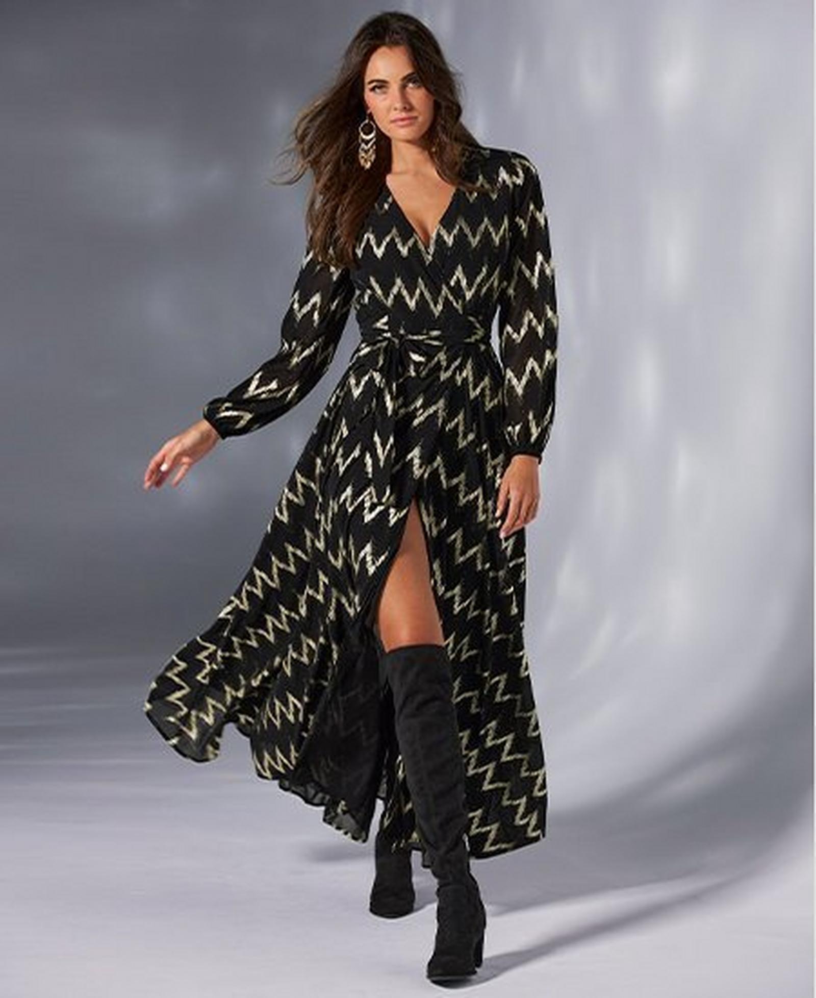 model wearing a black and gold chevron long-sleeve wrap maxi dress and black over-the-knee suede boots.