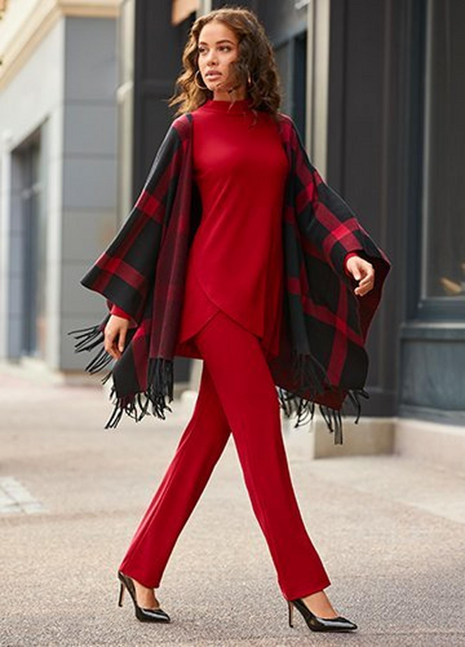 model wearing a red tulip hem mock-neck top, red straight leg pants, black and red plaid fringe poncho, and black pumps.