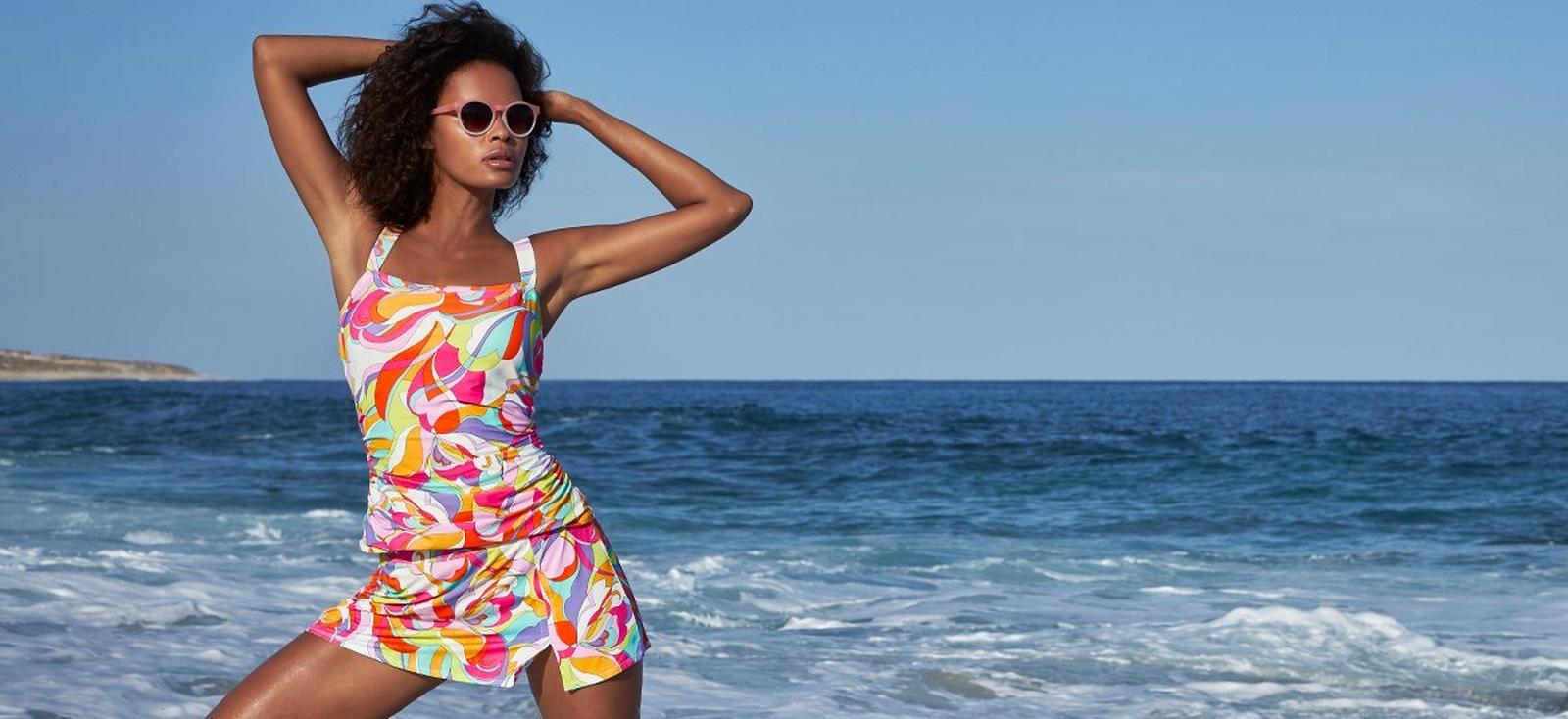 model wearing a sunset print tankini with skirted bottom and sunglasses.