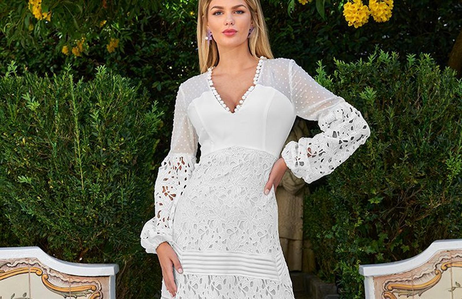 model wearing a white lace and pom-pom embellished long-sleeve maxi dress and purple flower earrings.