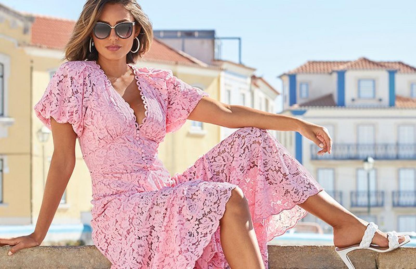 model wearing a pink lace short-sleeve maxi dress, sunglasses, silver hoop earrings, and white heeled sandals.