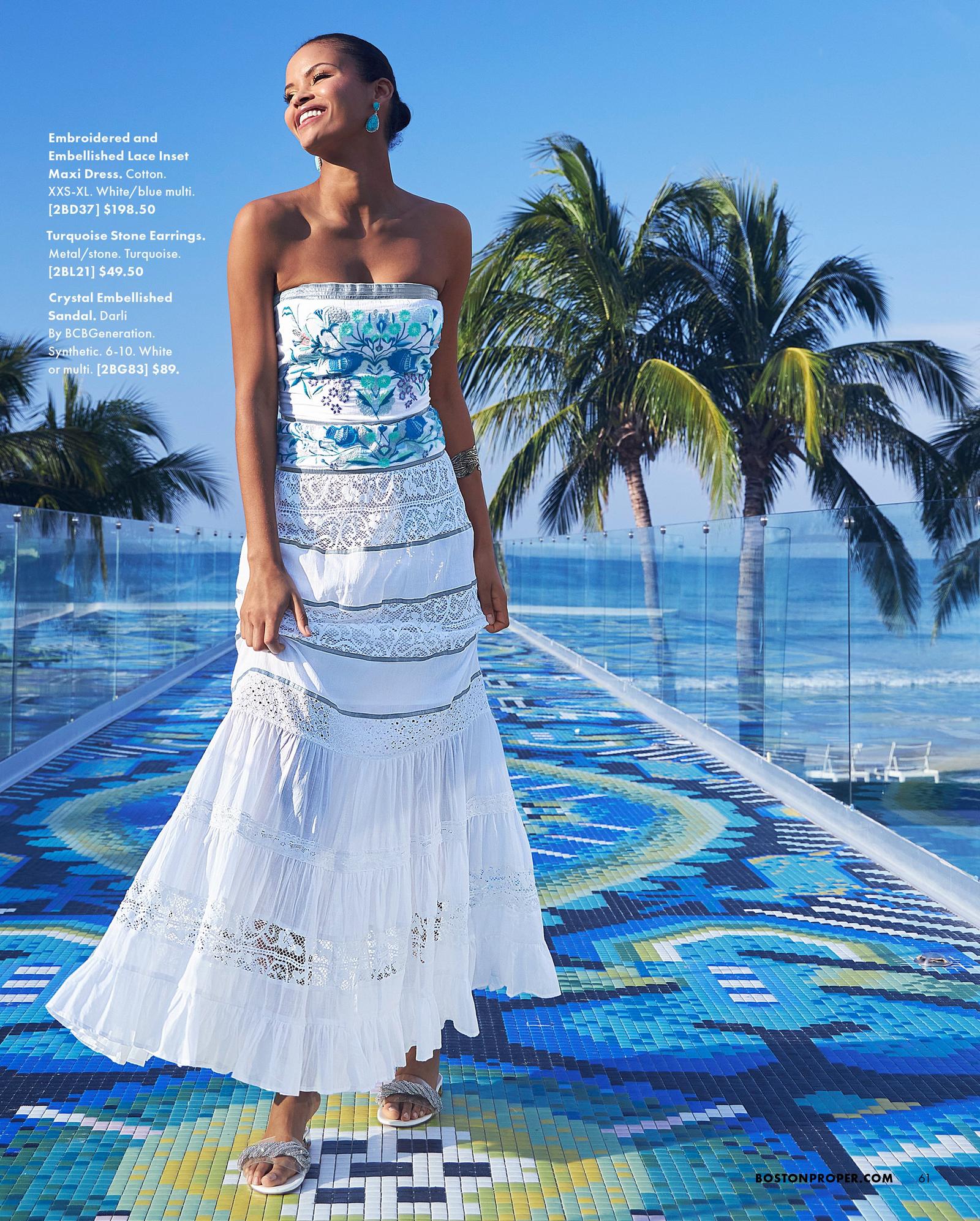 model wearing a blue and white embroidered and embellished strapless lace inset maxi dress, turquoise stone earrings, and crystal embellished sandals.