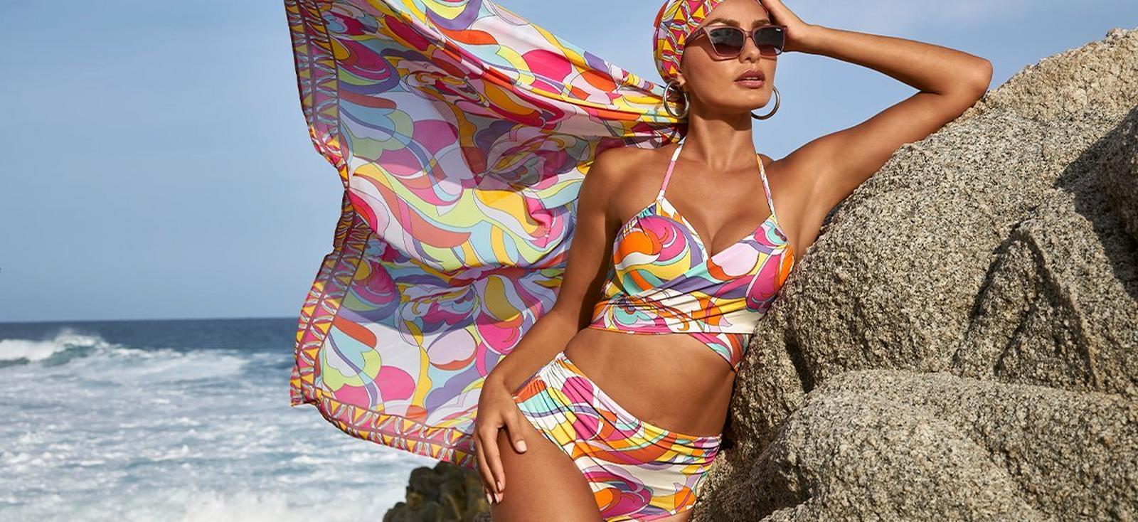 model wearing a paisley print multicolored high waisted bikini, sunglasses, and a pareo over her head.