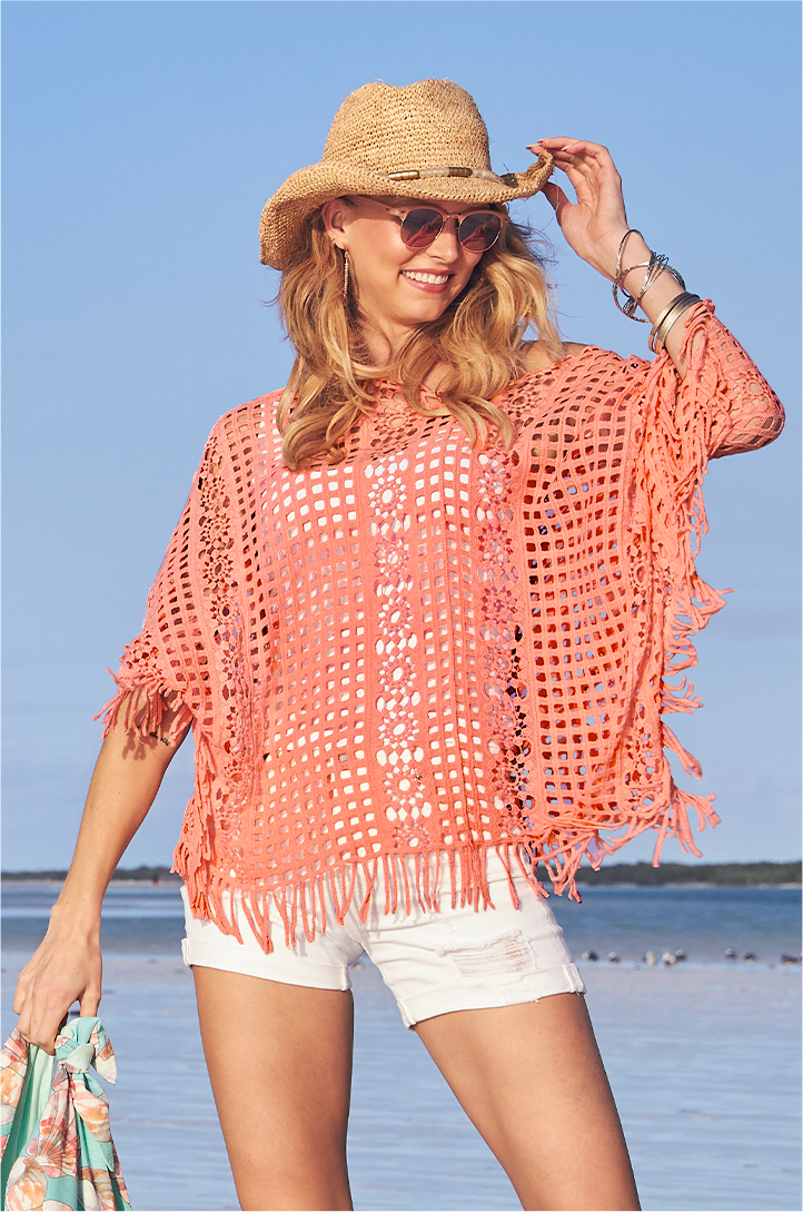 model wearing a pink crochet poncho, white tank top, white denim shorts, sunglasses, and embellished cowboy hat.