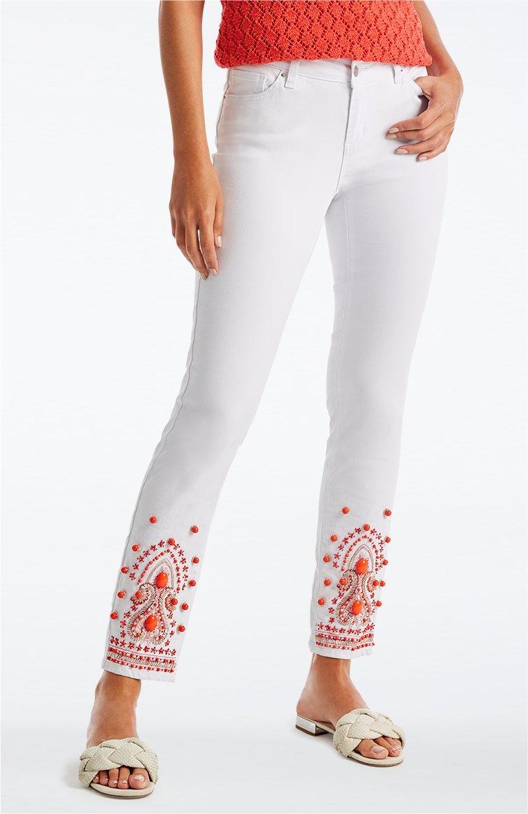model wearing white jeans with coral embroidery at the bottom, white braided slides, and a coral crochet top.
