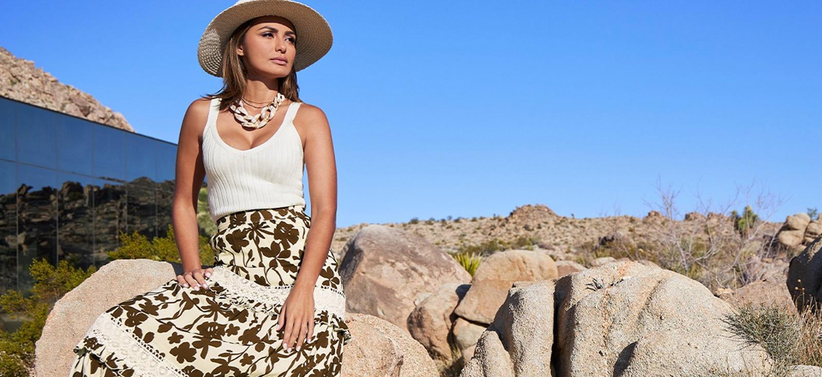 model wearing an off-white ribbed sweater tank top, wide brim tan hat, statement necklace, brown and white lace maxi skirt.