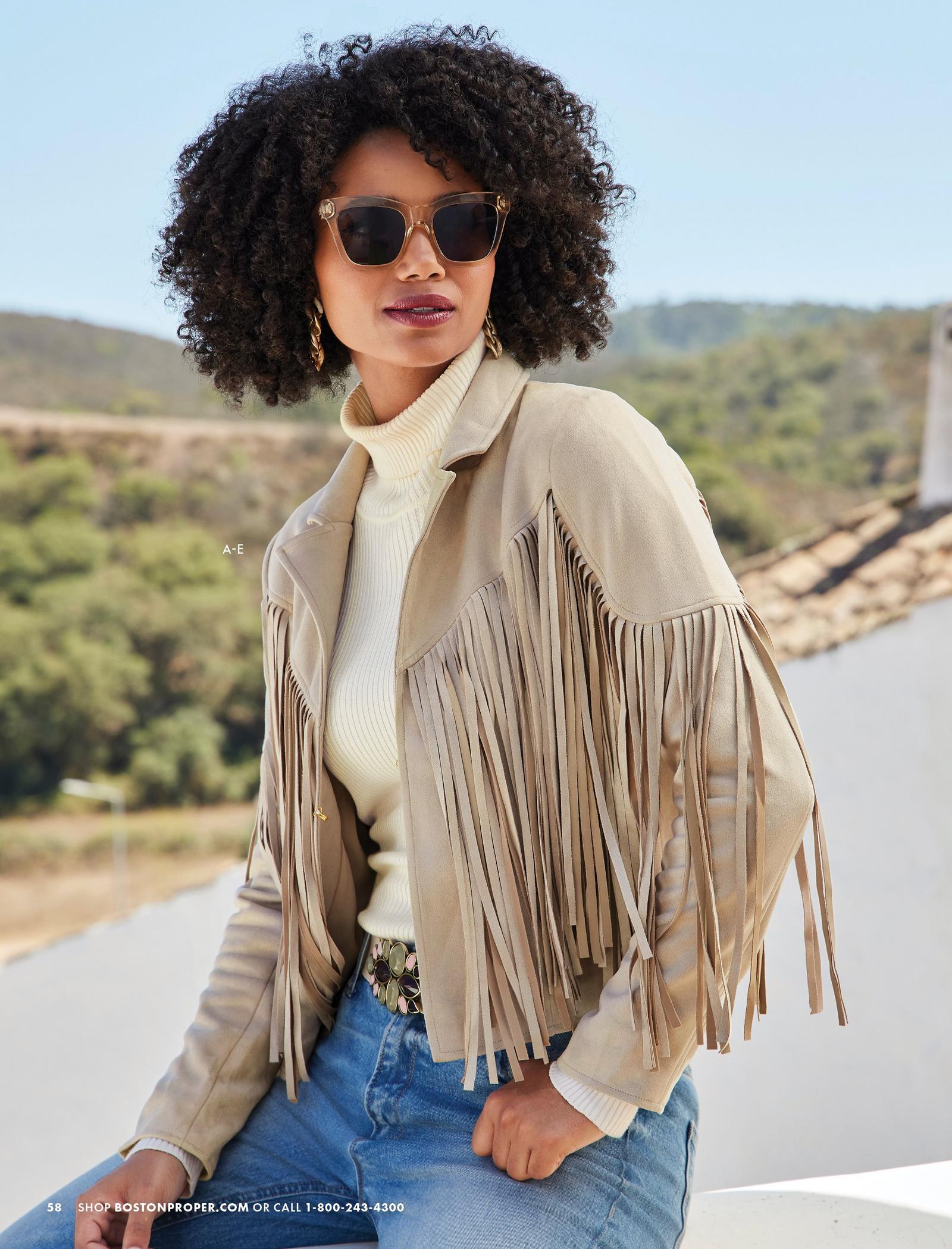 model wearing a tan fringe faux-suede jacket, off-white ribbed turtleneck sweater, stone embellished belt, jeans, gold chain earrings, and sunglasses.